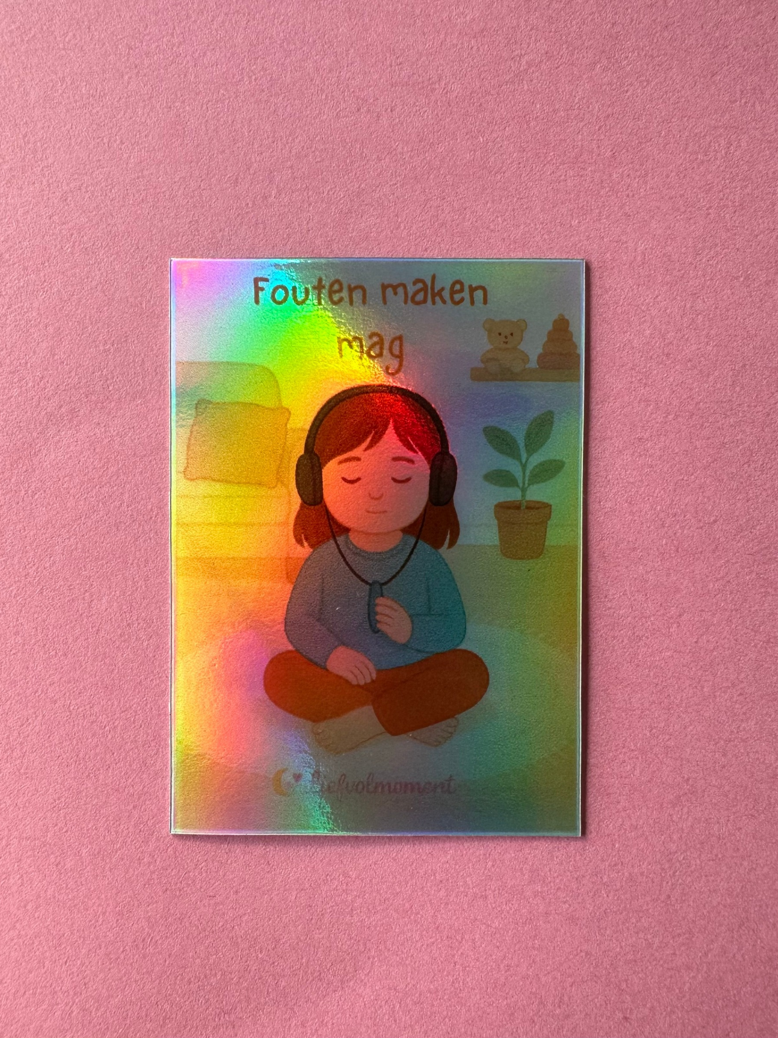 Een holografische sticker toont een persoon die in een meditatieve houding zit met een koptelefoon op, met het opschrift 