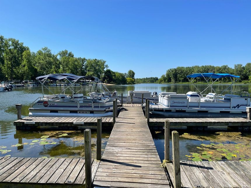 A row of pontoon boats are docked at a dock on a lake.