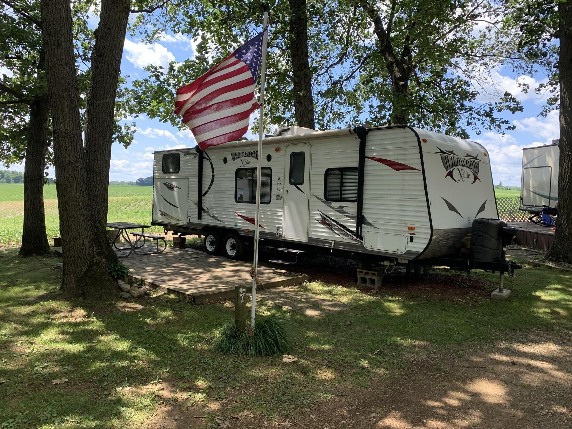 A rv is parked in a grassy area with an american flag flying in the background.