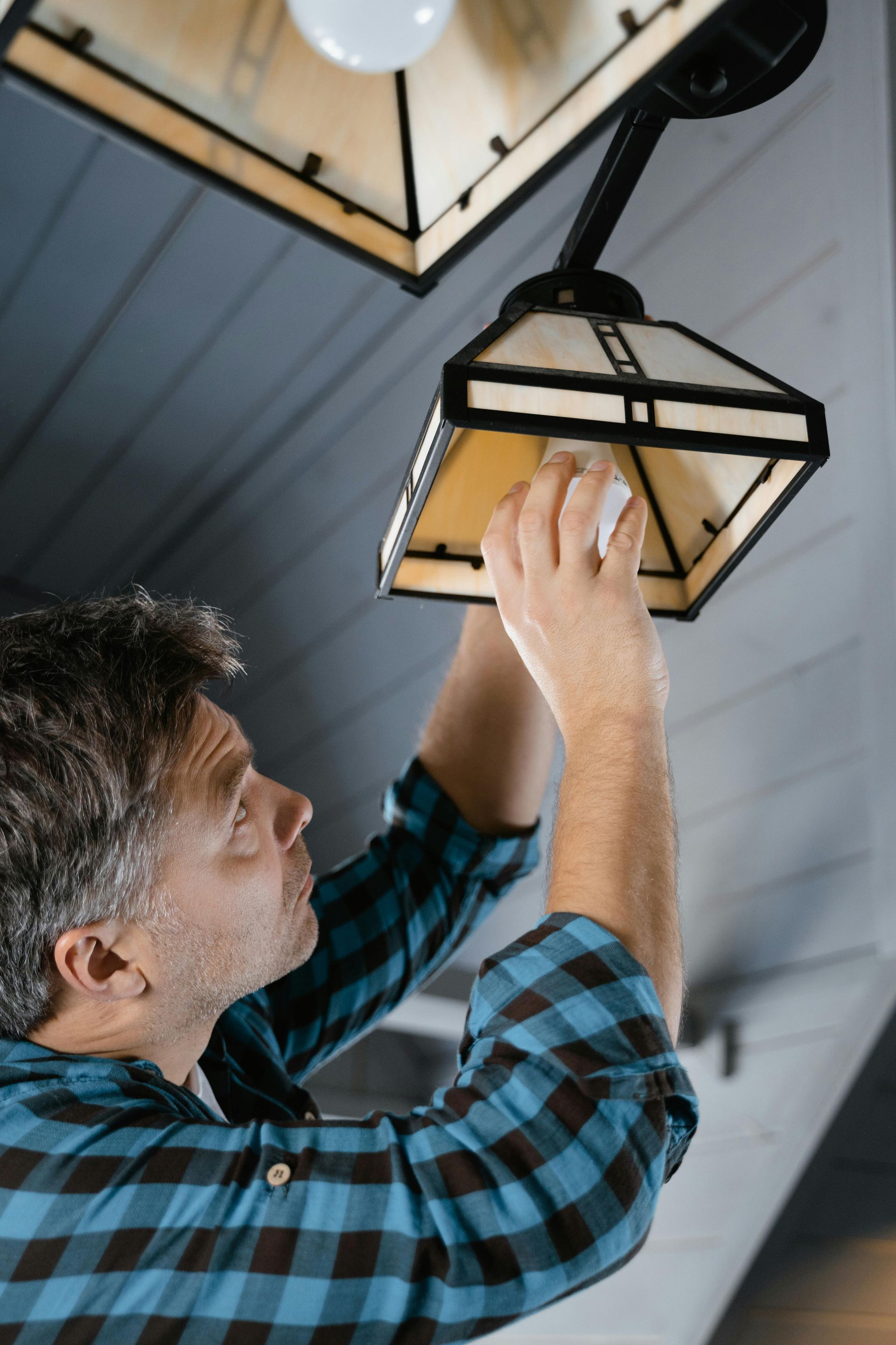 A man is fixing a light fixture on the ceiling.