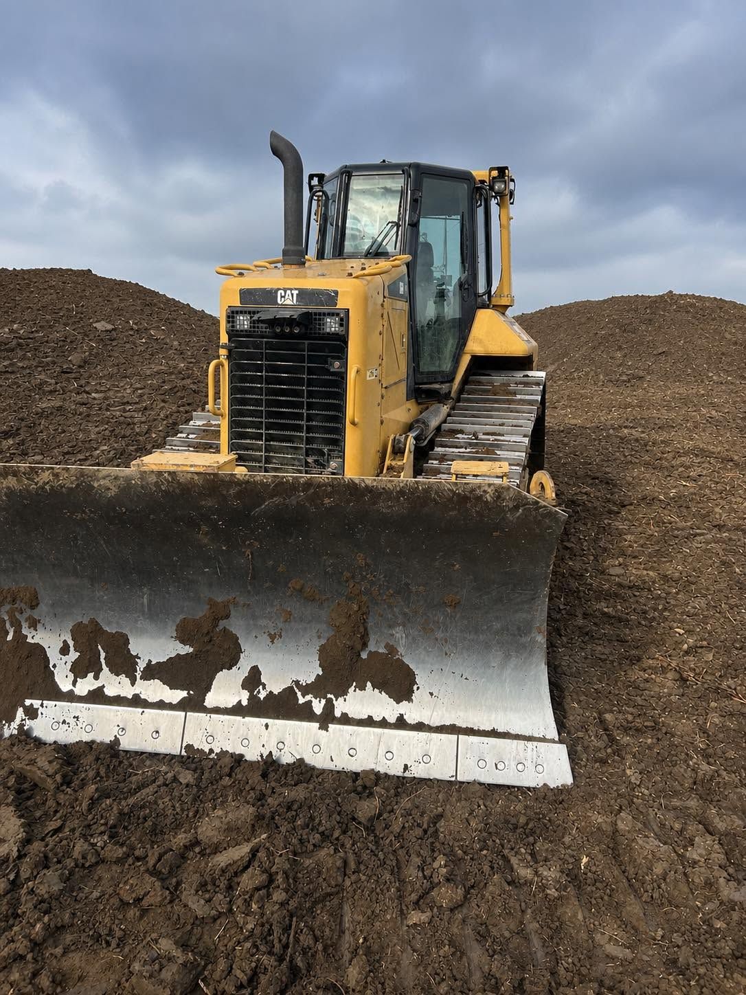 Yellow bulldozer pushing dirt in a dirt lot, with a large blade and tracks visible.