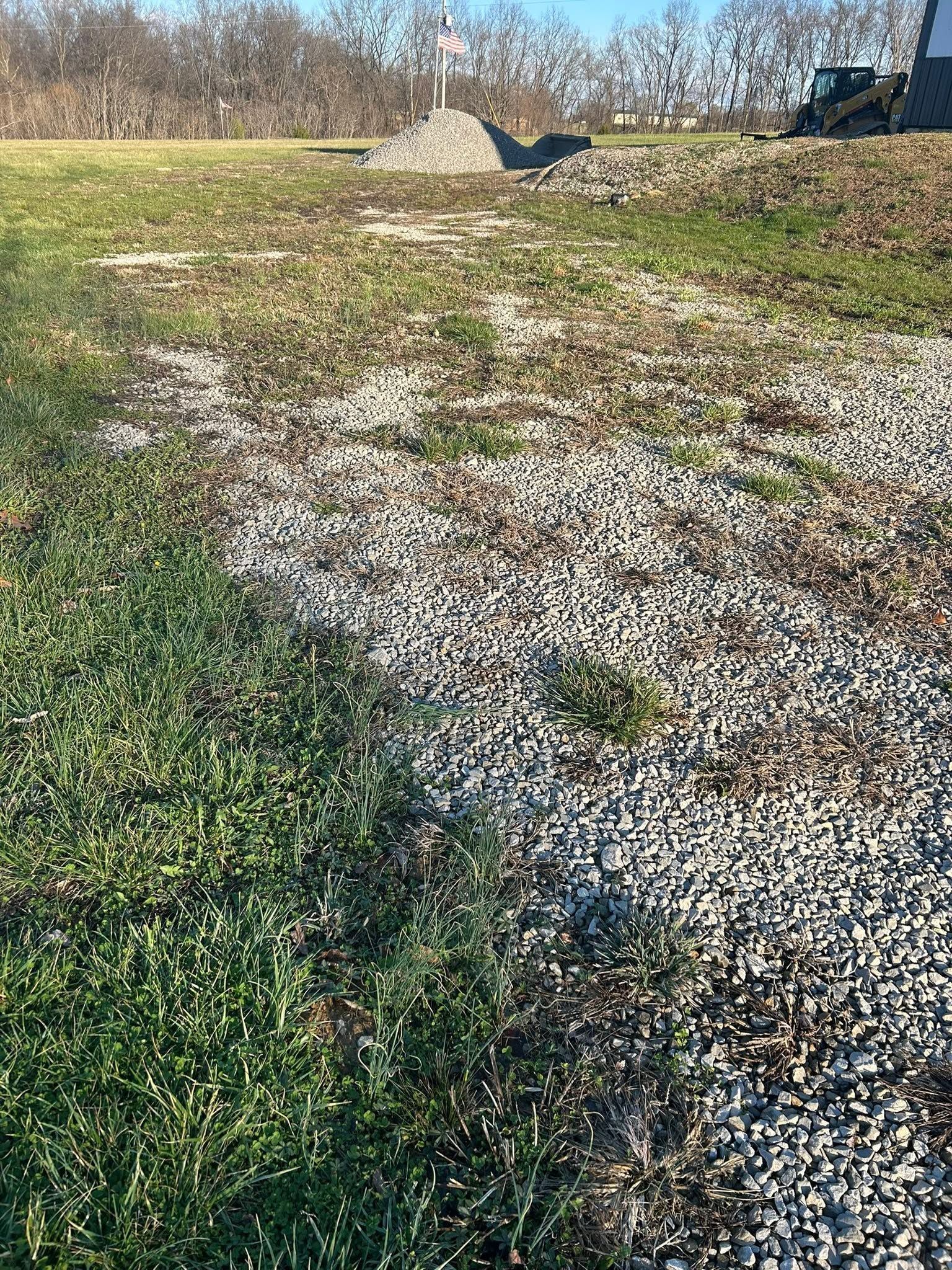 Gravel path through grassy field under clear blue sky, with a large rock and utility pole in the distance