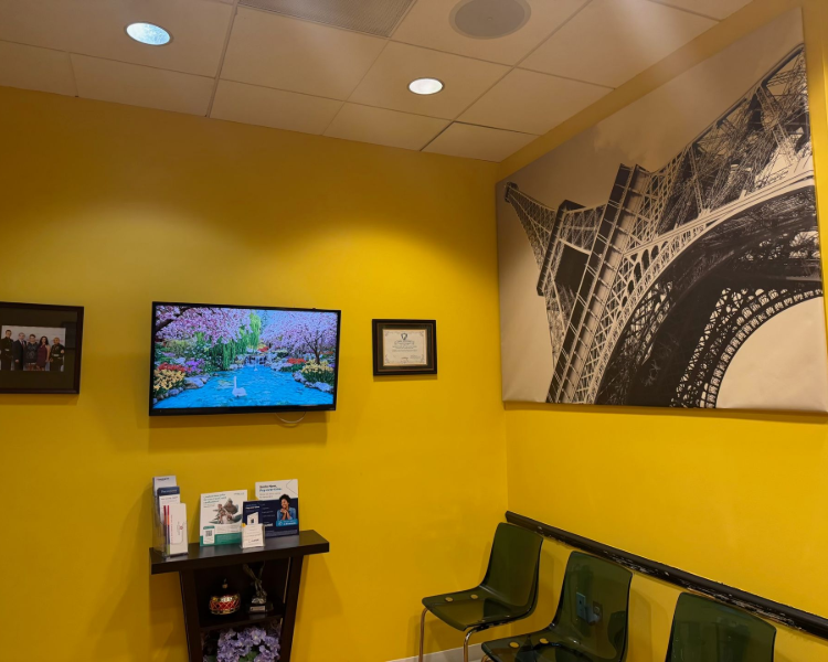 Bright yellow waiting room with TV, brochure stand, green chairs, and large black-and-white wall art.
