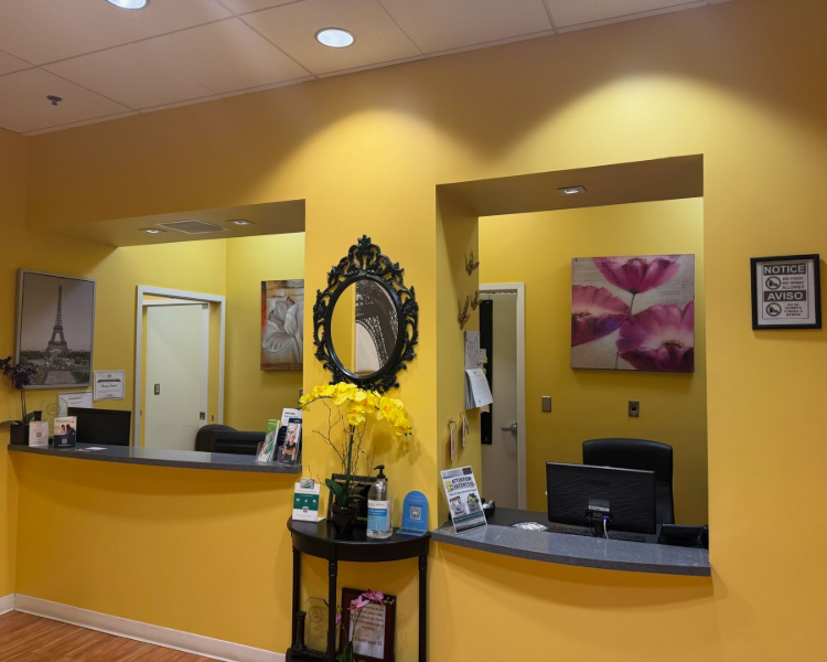 Yellow reception desk with computer monitors, wall mirror, and flower arrangement in a lobby.