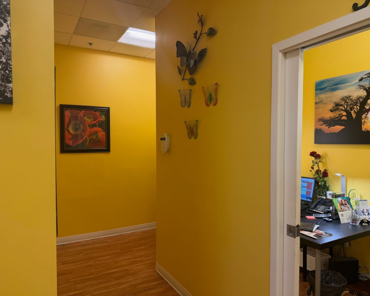 Yellow hallway with framed art and butterfly wall decor, leading to a doorway into a home office.