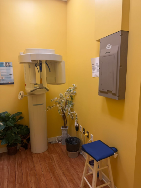 Dental X-ray room with yellow walls, X-ray machine, potted plants, and a blue stool