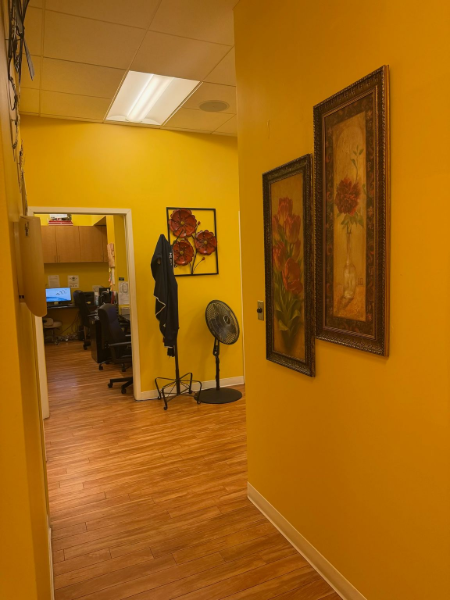 Yellow hallway with framed wall art, a standing fan, and an open doorway to another room