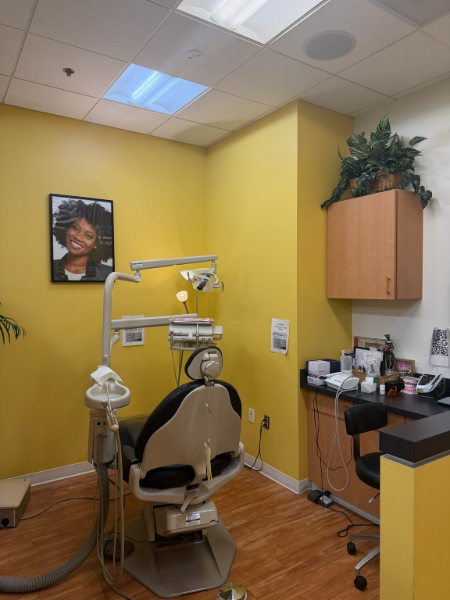 Dental exam room with yellow walls, patient chair, overhead lamp, and cabinets.