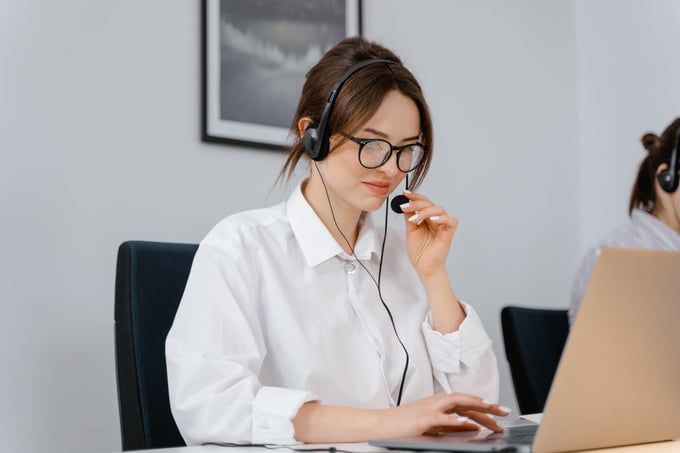 A woman wearing a headset is sitting in front of a laptop computer.