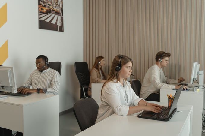 A group of people are sitting at desks in front of computers in a call center.