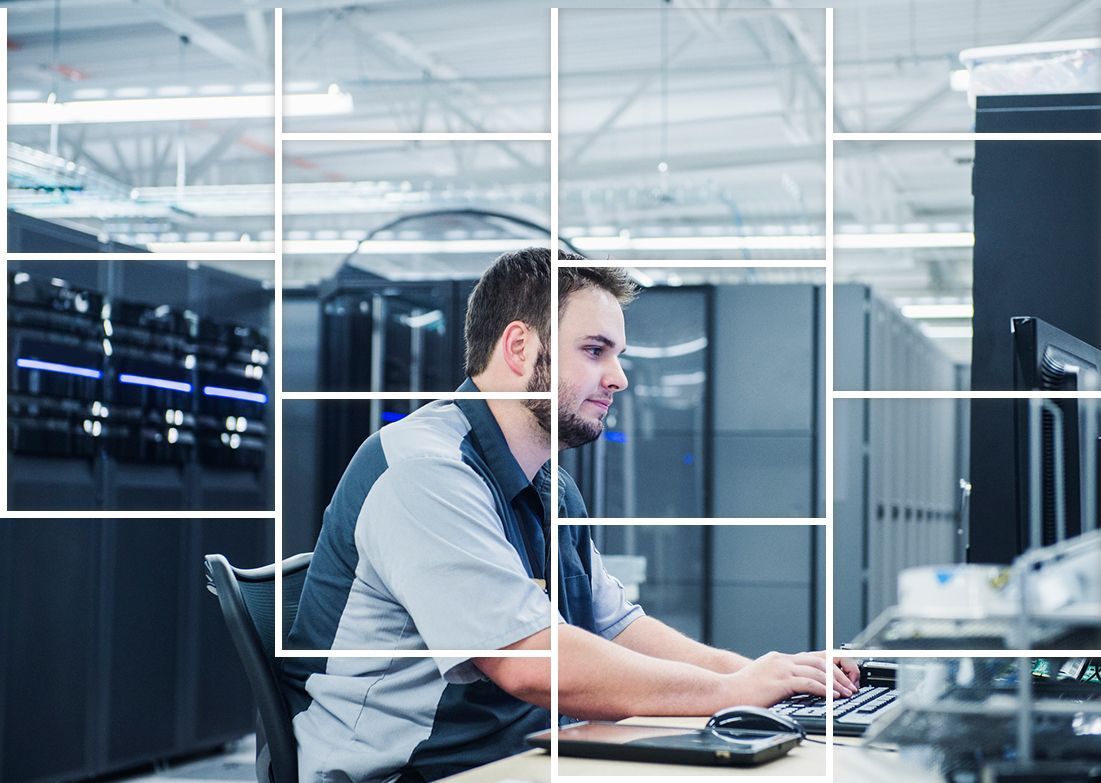 A man is sitting at a desk in front of a computer in a server room. A man is sitting at a desk in front of a computer in a server room.