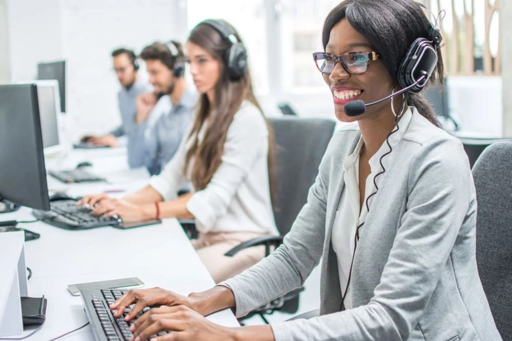 A woman wearing a headset is typing on a computer in a call center. A woman wearing a headset is typing on a computer in a call center.