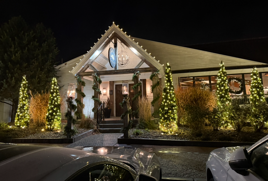 Illuminated brick building entrance at night with holiday lights and parked cars in front