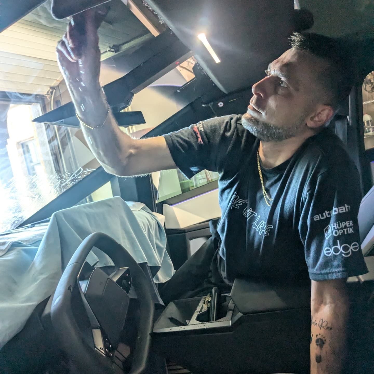 A man is sitting in a car looking under the hood.