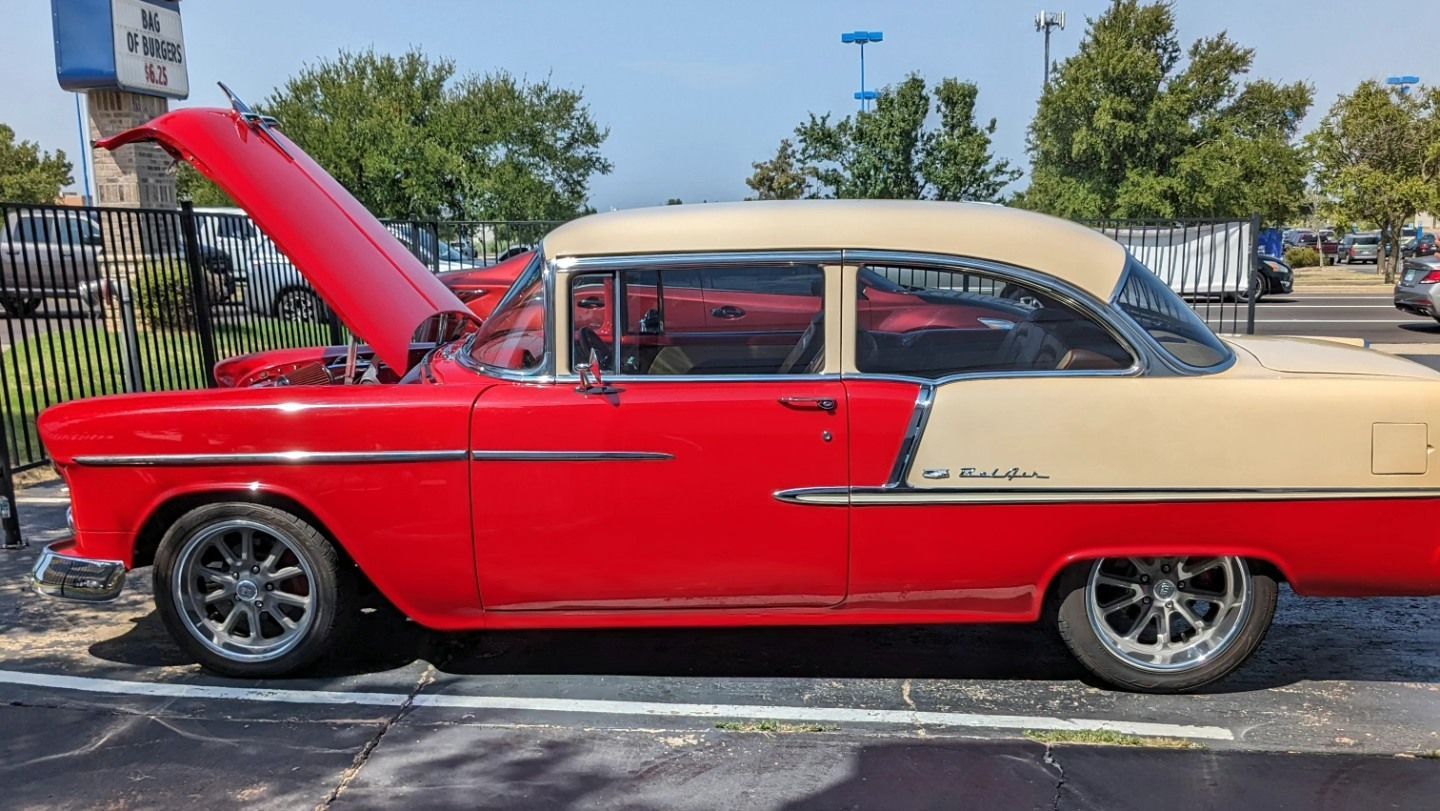 A red and white car with the hood up is parked in a parking lot