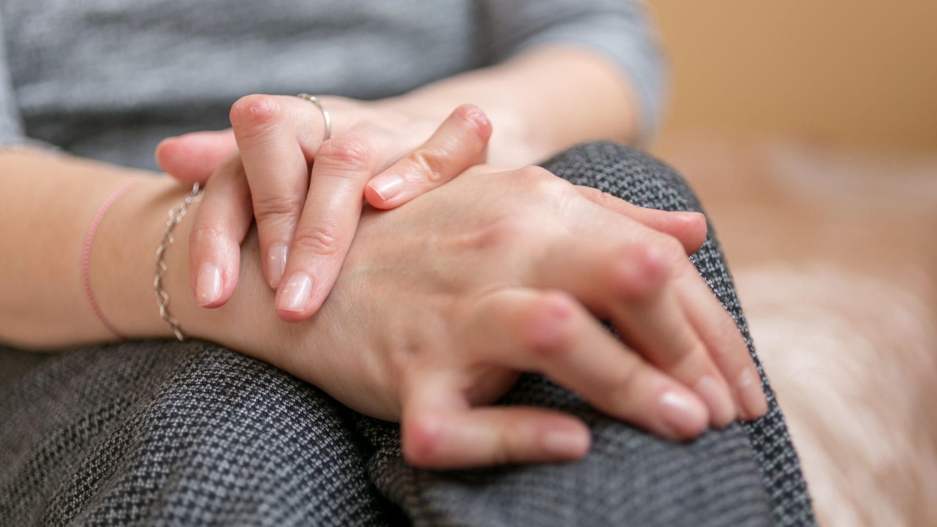 Close-up of two hands resting together on a knee, with a bracelet visible and soft indoor lighting.