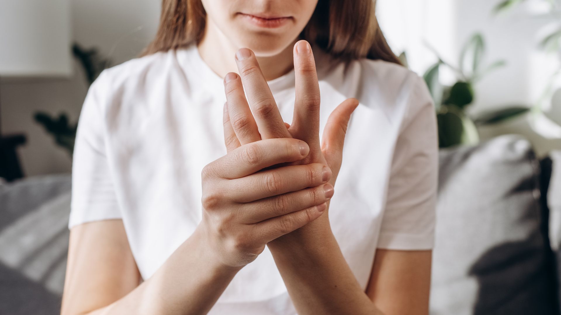 Person in a white shirt holding and examining a bent finger on a couch