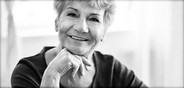 Black and white closeup photo of a woman with her chin resting on her right hand smiling