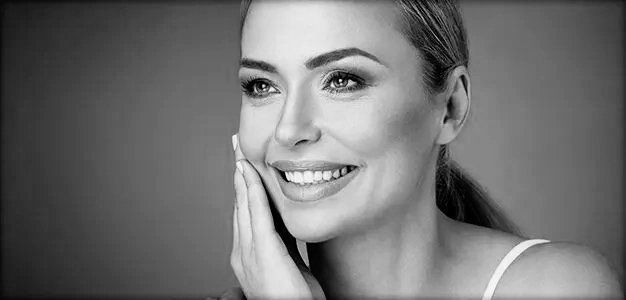 Black and white portrait of a woman smiling touching her face with one hand smiling after getting a face and neck lift