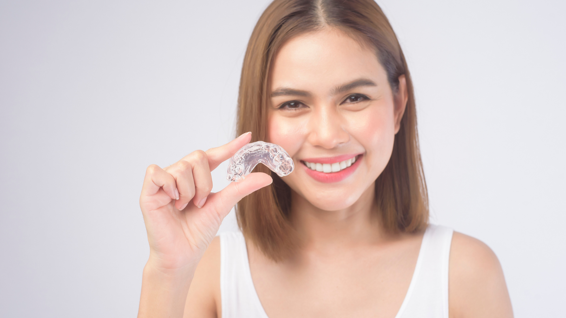 A woman is holding a clear brace in her hand and smiling.