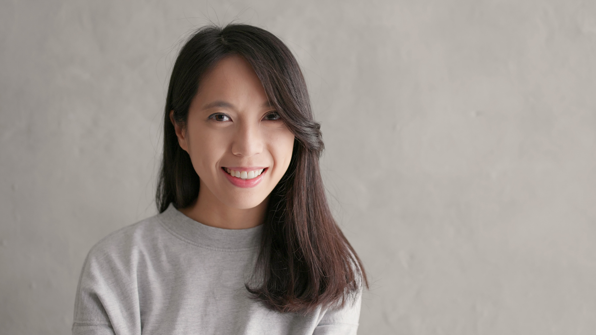 A woman in a grey sweater is smiling and looking at the camera.