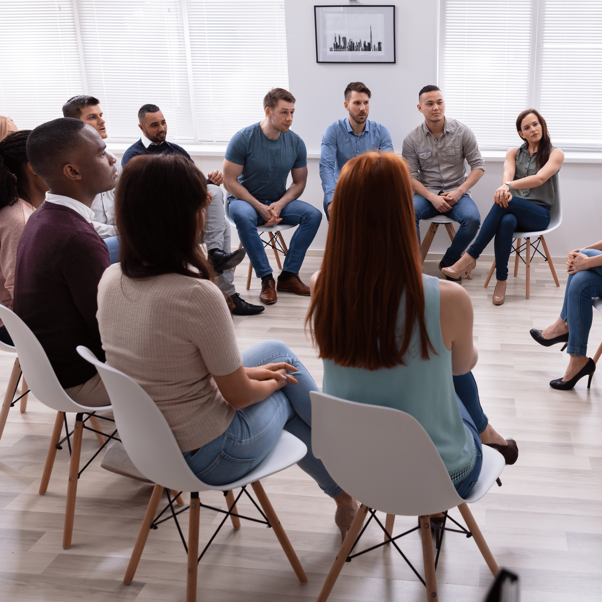 Group therapy session with diverse people seated in a circle, listening to a person talking.