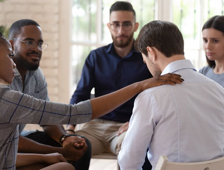 Group therapy session: person consoled by another, hand on shoulder; others watch supportively.