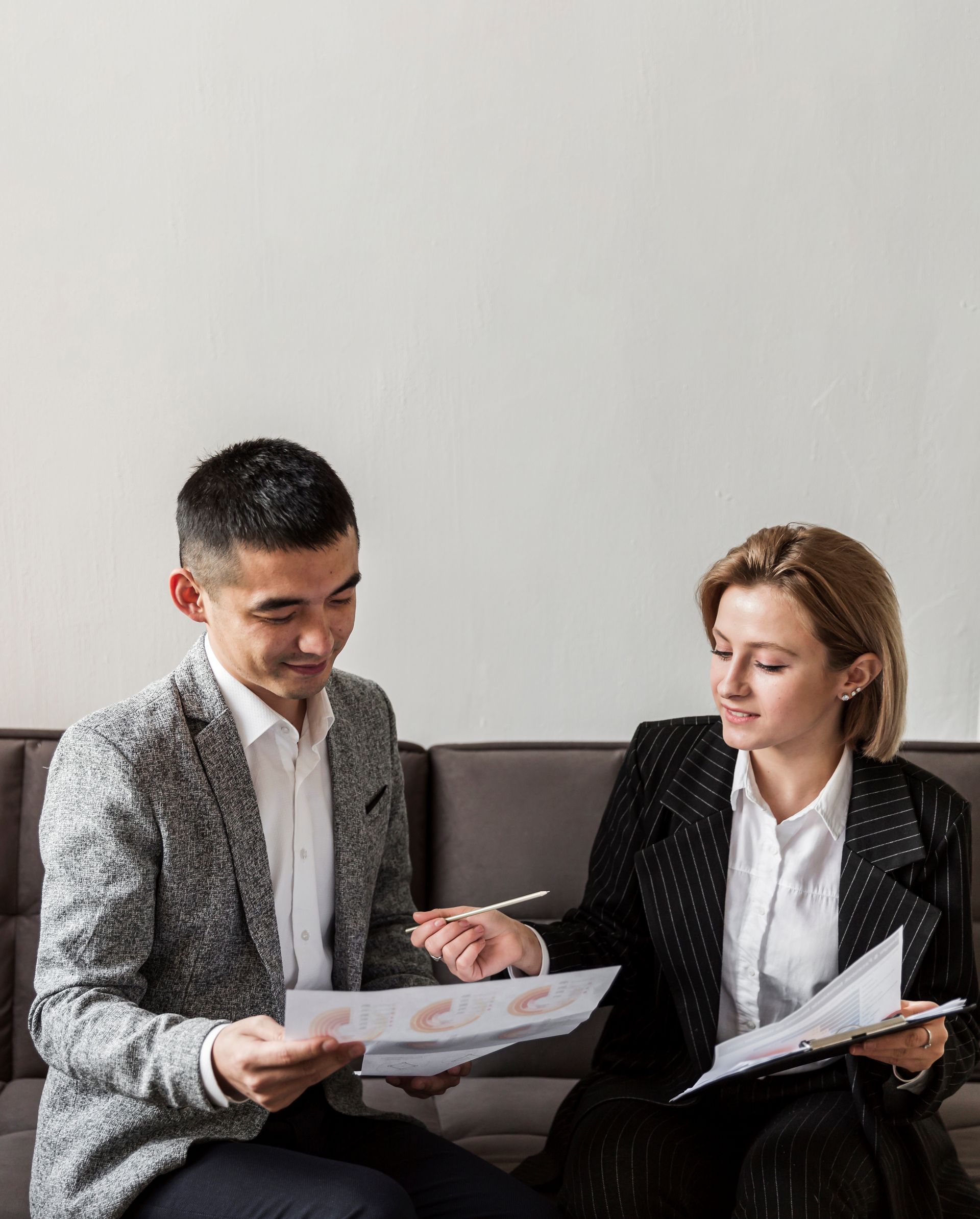 Two people in business attire reviewing documents on a couch, indoors.
