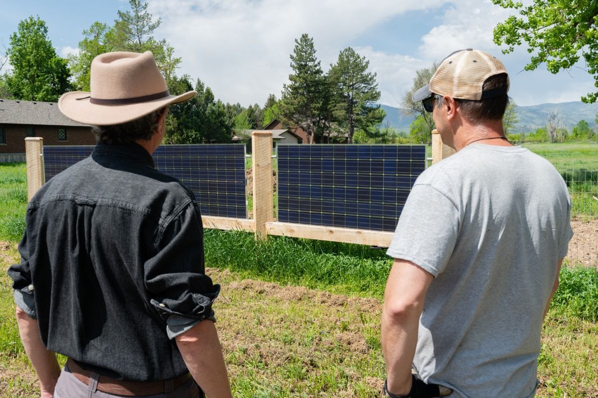 Two men are standing in a field looking at solar panels.