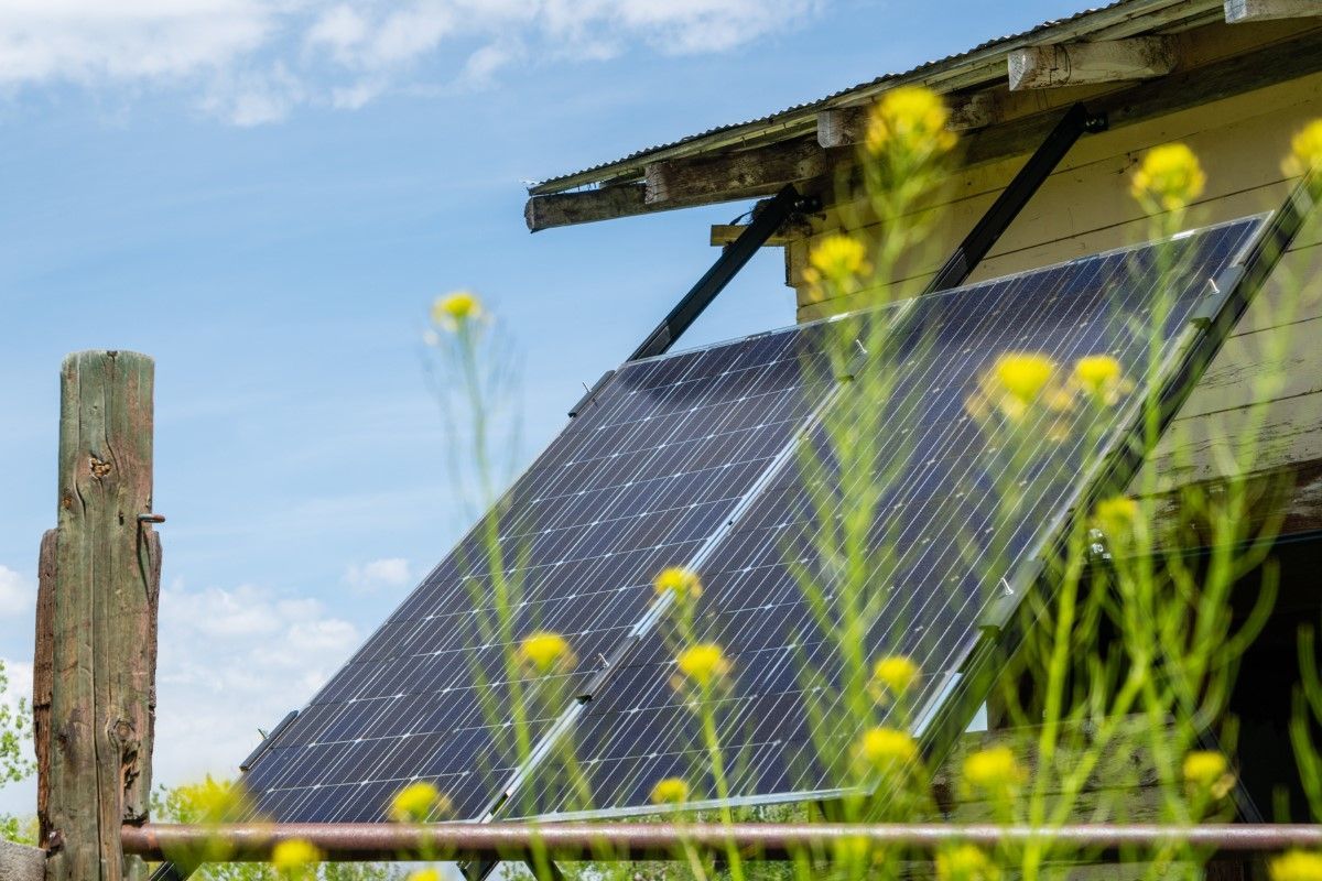 A solar panel is mounted on the side of a building next to a wooden fence.