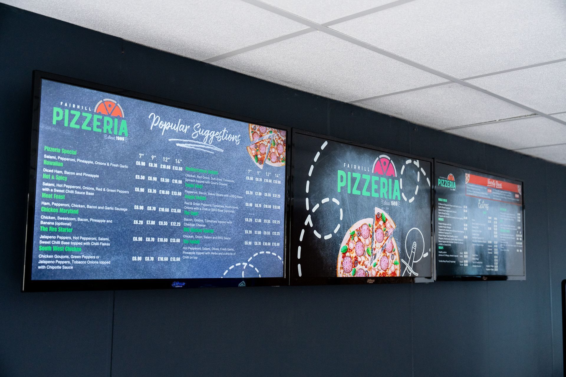 A chalkboard menu for a pizzeria is hanging on a wall.