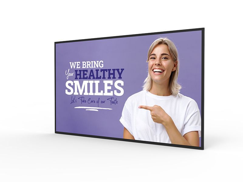 A woman is pointing at a sign that says `` we bring your healthy smiles ''.