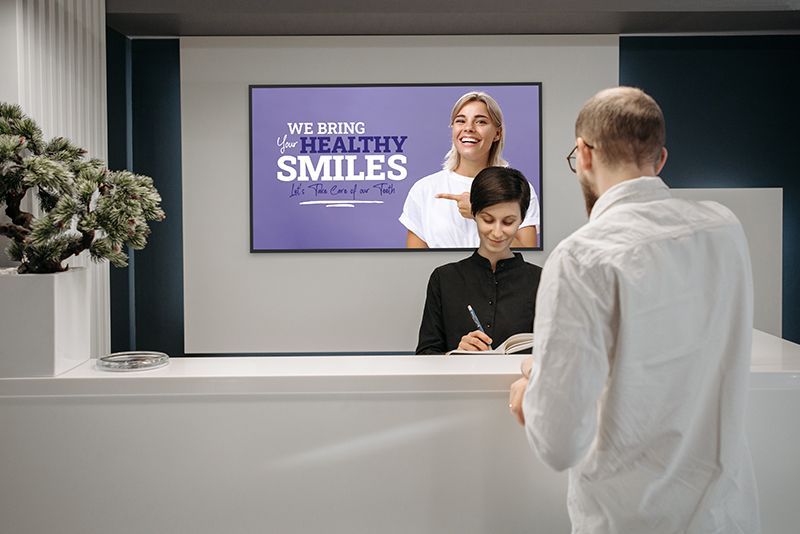 A woman is pointing at a sign that says `` we bring your healthy smiles ''.