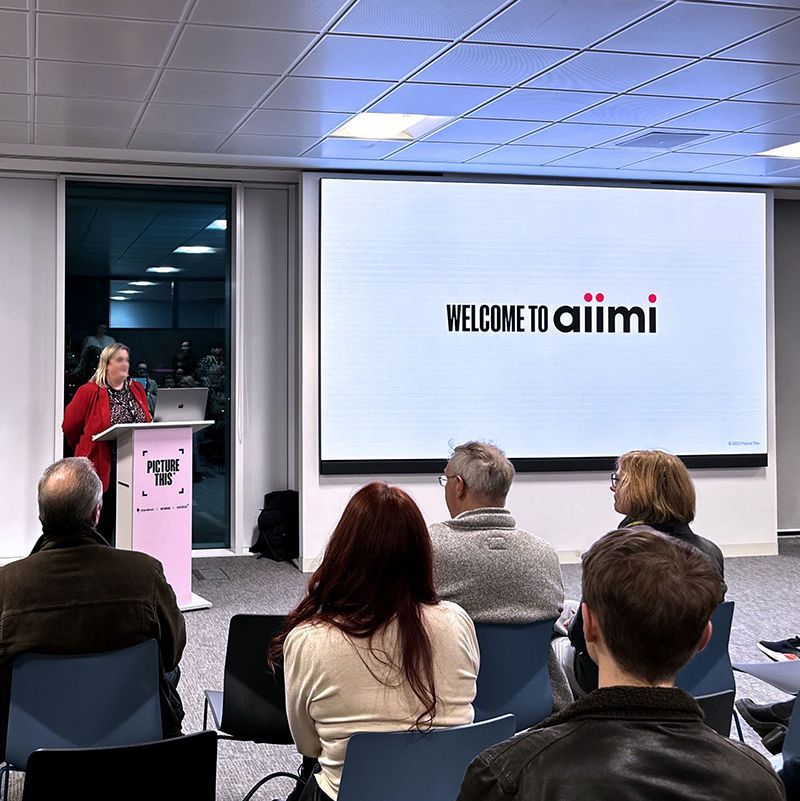 A group of people are sitting in front of a screen that says welcome to aiimi