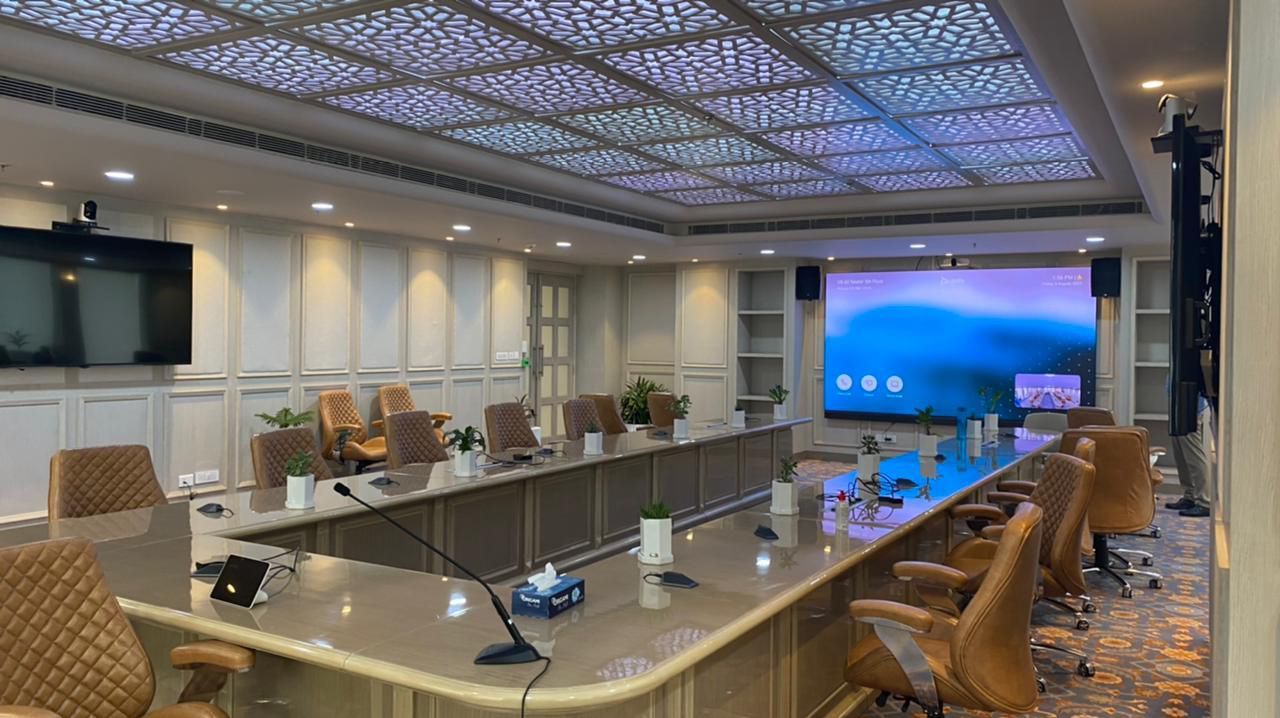 A conference room with a long table and chairs and a large screen.