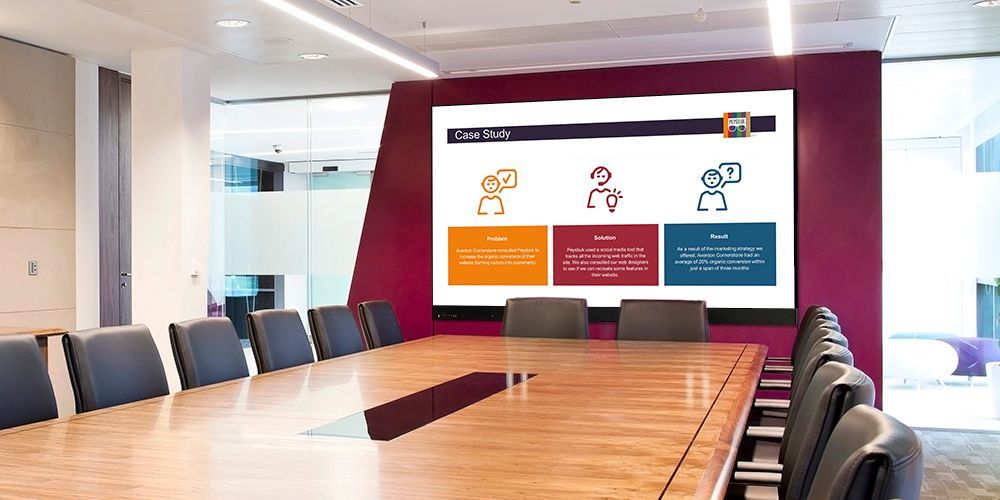 A conference room with a long table and chairs and a large screen on the wall.