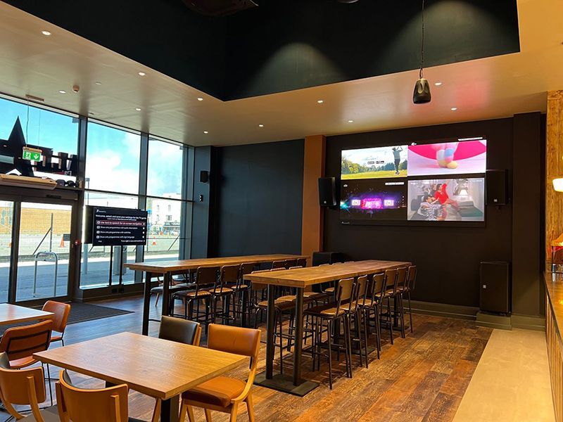A restaurant with tables and chairs and a large screen on the wall.