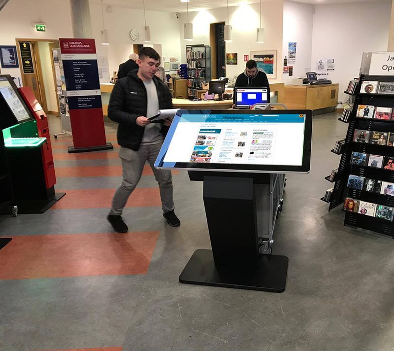 A man is standing in front of a large screen in a library