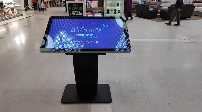 A large touchscreen display is sitting in the middle of a mall.