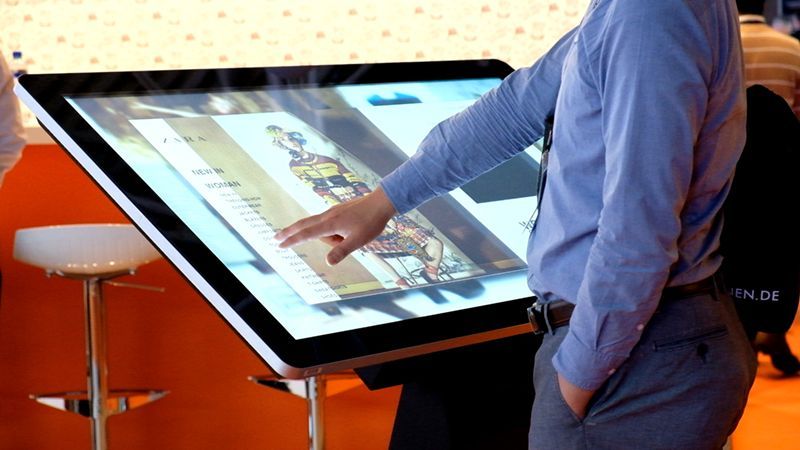 A man in a blue shirt is touching a large screen