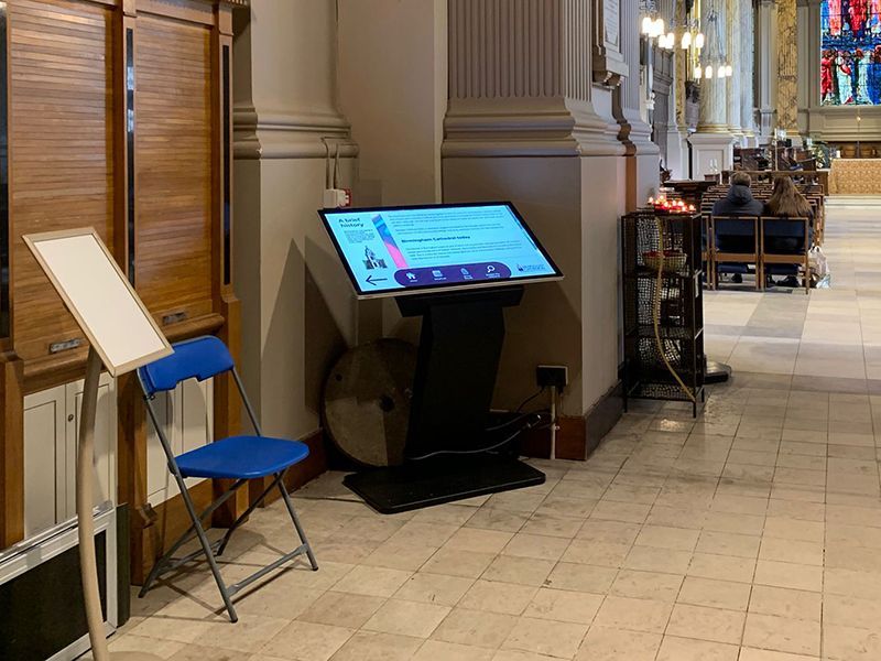 A large flat screen tv is sitting next to a blue folding chair in a church.