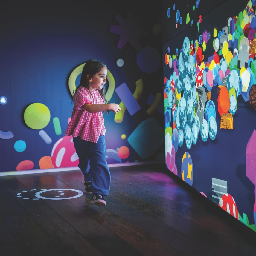 A little girl is standing in front of a large screen