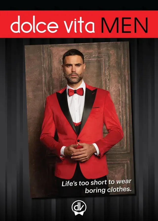 A man wearing a red tuxedo jacket and bow tie stands against a dark background.