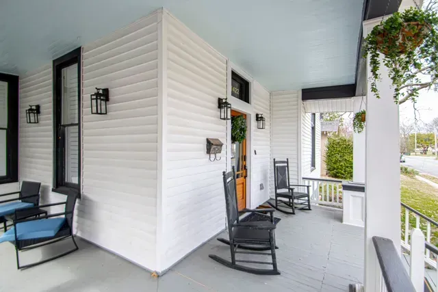 White porch with light blue ceiling, black rocking chairs, and wall-mounted black lanterns.
