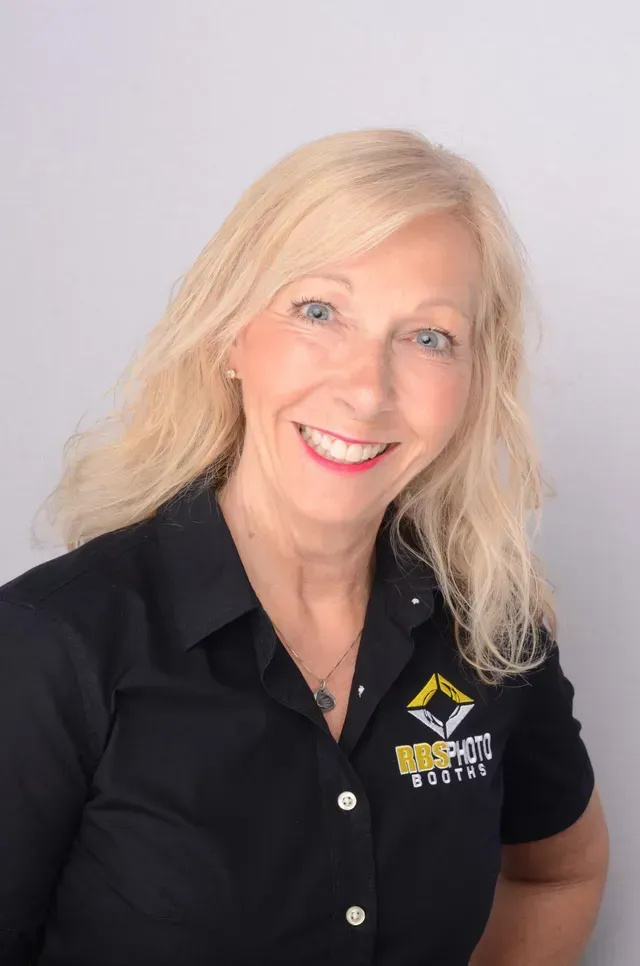 Smiling professional with blonde hair wearing a black polo shirt with a company logo, set against a light gray background.