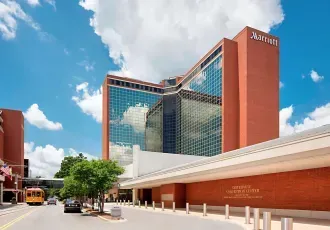 The Marriott hotel building with a brick exterior and glass facade under a blue sky, viewed from a street with a bus.