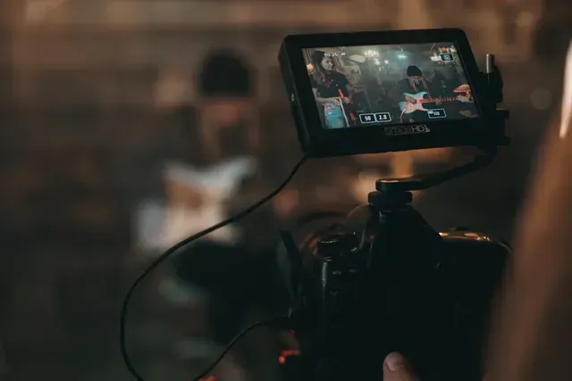 A camera films a musician playing an electric guitar in a dimly lit, professional studio setting.