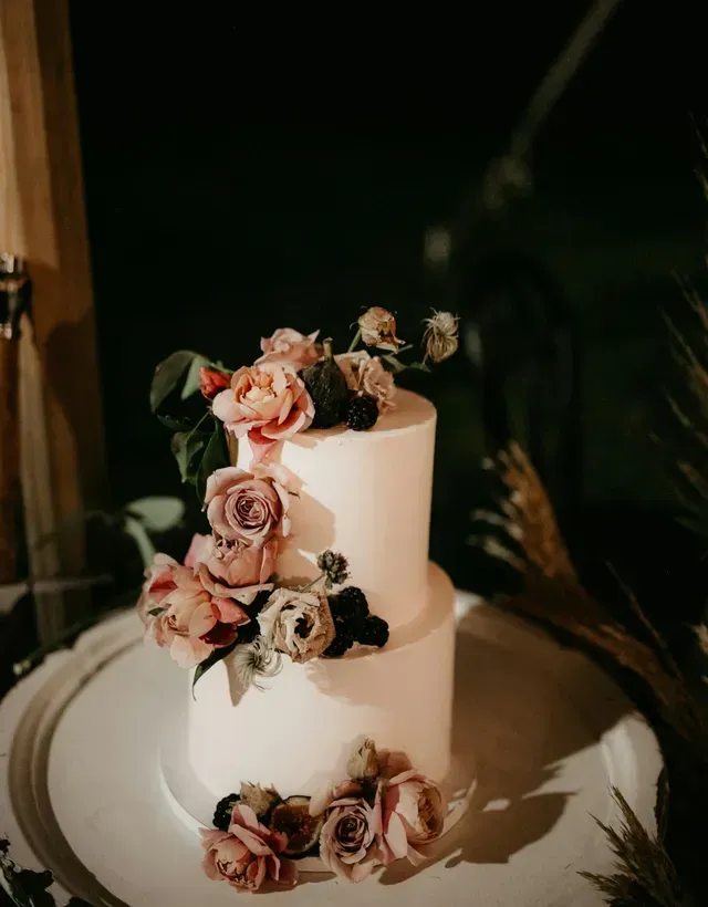 Two-tiered white wedding cake adorned with cascading pastel roses and greenery on a round serving platter.