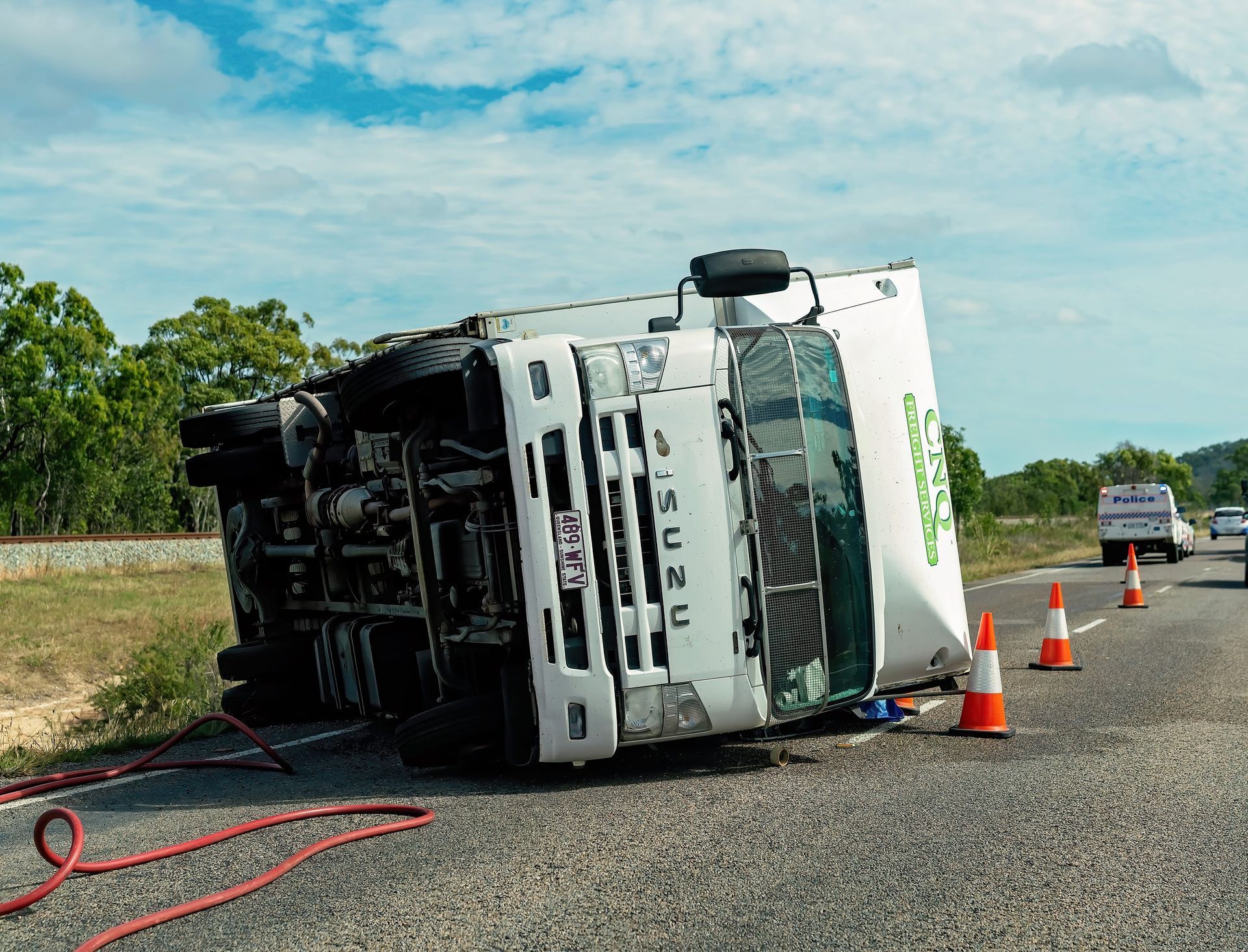 Overturned white truck on roadside with traffic cones and hoses