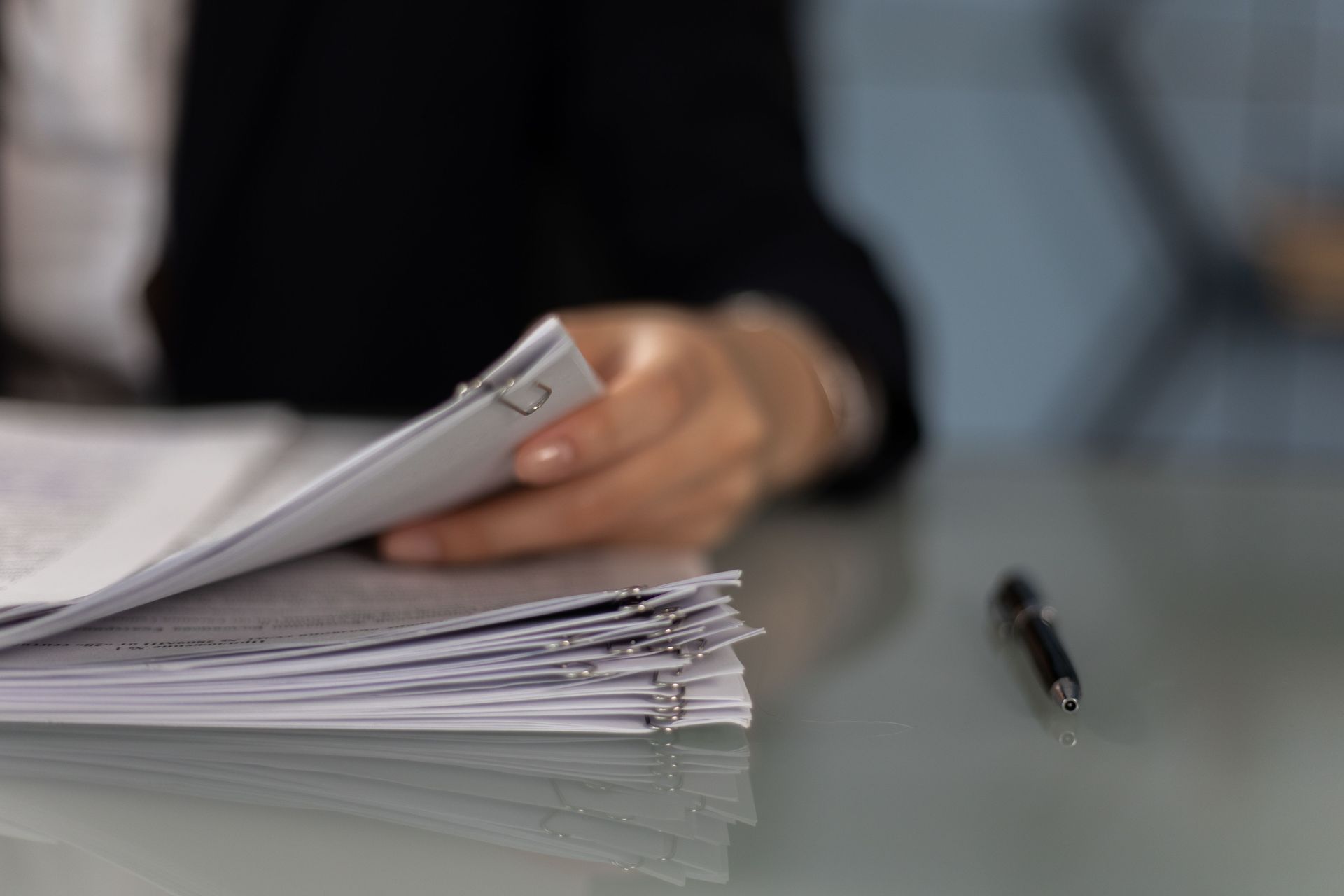 Hand flipping through a stack of papers beside a pen on a desk